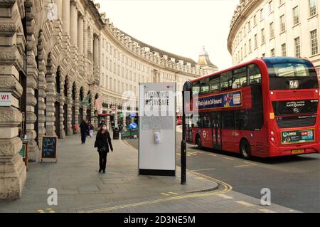 Una donna con una maschera protettiva passa accanto a un cartello di distanziamento sociale Stay Safe e dispenser di disinfettante per le mani su Regent Street, Londra, Regno Unito 2020 Foto Stock