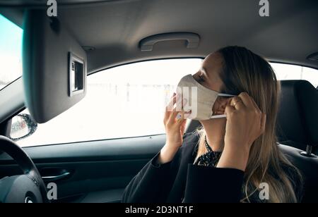 Giovane Businesswoman che mette sulla maschera di faccia in automobile prima di andare Al lavoro in ufficio Foto Stock