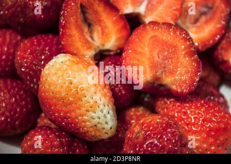 Primo piano di fragole, intere e tagliate a fette. Mature e immature, bianche e rosse, opposizione. Sfondo Foto Stock