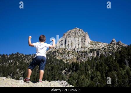 Giovane ragazzo che fa il gesto della vittoria guardando un grande montagna Foto Stock