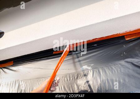 Uno strato appena applicato di intonaco di silicone sul montante della finestra, la finestra è fissata con foglio nero, staccando il nastro arancione. Foto Stock