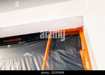 Uno strato appena applicato di intonaco di silicone sul montante della finestra, la finestra è fissata con foglio nero, staccando il nastro arancione. Foto Stock