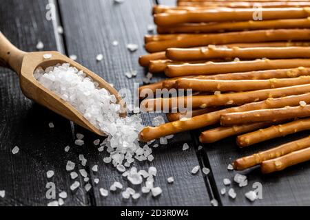 Bastoncini salati. Pretzel croccanti e sale grosso in paletta di legno. Foto Stock