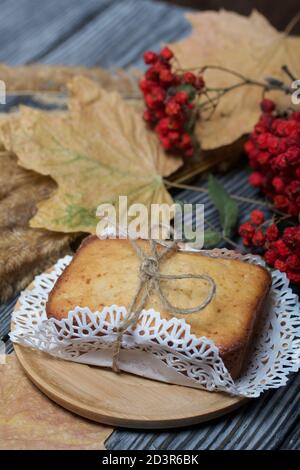 Cupcake appena sfornato su un tovagliolo. Legato con spago. Nelle vicinanze si trova un ramo di rowan secco con bacche rosse e foglie d'acero. Sullo sfondo del nero Foto Stock