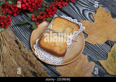 Cupcake appena sfornato su un tovagliolo. Legato con spago. Nelle vicinanze si trova un ramo di rowan secco con bacche rosse e foglie d'acero. Sullo sfondo del nero Foto Stock