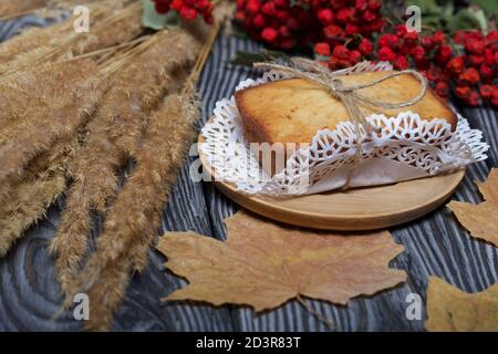 Cupcake appena sfornato su un tovagliolo. Legato con spago. Nelle vicinanze si trova un ramo di rowan secco con bacche rosse e foglie d'acero. Sullo sfondo del nero Foto Stock