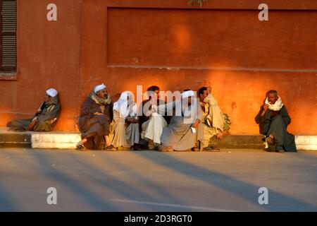 Nelle strade della città di Luxor, il ritmo della vita è calmo. Uomini arabi seduti su un podio accanto al muro di una casa Foto Stock