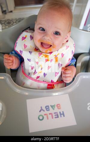 Bambino sorridente di 6 mesi coperto di purea di carote Foto Stock