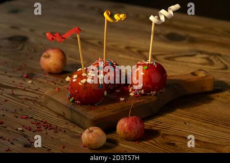 Mele in caramello rosso, decorate con decorazioni su una tavola di legno su sfondo scuro. Concetto di cibo festivo. Foto Stock