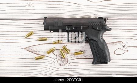Semplice pistola a pistola moderna nera con pochi proiettili in ottone giallo su tavola di legno bianco, vista dall'alto Foto Stock