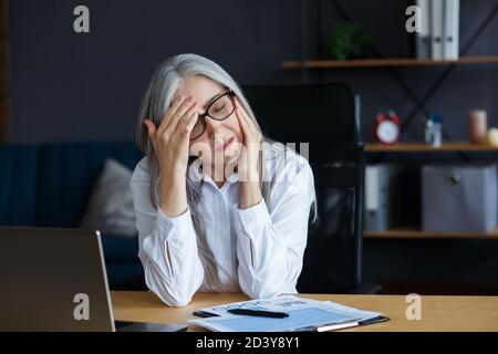 Burnout e overwork concept.stanco imprenditore che lavora straordinario in Office.Portrait di Donna anziana con capelli grigi stressati con strain testa. Occhio Foto Stock
