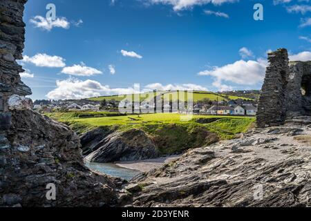 Vista attraverso le antiche rovine sulla spiaggia rocciosa tra le scogliere con vecchie fortificazioni navali, cannoni e villaggio di Wicklow sullo sfondo, Irlanda Foto Stock