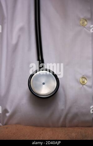 Primo piano di uno stetoscopio appeso su un pulsante bianco camicia che fa parte dell'uniforme di un medico Foto Stock