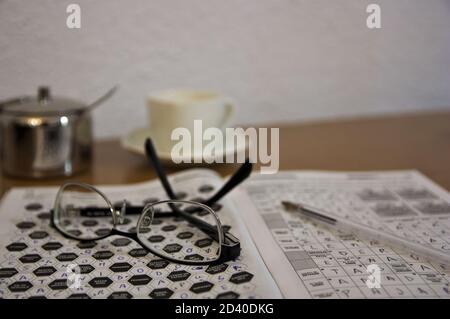 Primo piano di alcuni occhiali da lettura e alcune crosswords che qualcuno fa da hobby mentre si ha un caffè Foto Stock