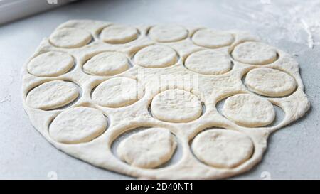 Preparazione dell'impasto per la cottura, il congelamento, lo scolpimento e altri sbozzati alimentari - un grosso pezzo di impasto è sul tavolo e lo chef taglia la puzzatura Foto Stock