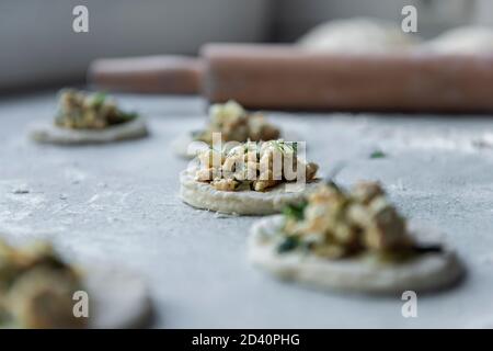 Una delle fasi di produzione di gnocchi di carne - sopra la tavola su un pezzo di impasto è una carne ripieno di verde accanto ad un cumulo di farina Foto Stock