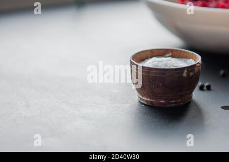 Cottura delle spezie - sale marino in un contenitore di legno pepe nero di pisello sul tavolo. Messa a fuoco frontale e posteriore selettiva Foto Stock