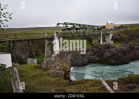 Un piccolo ponte di metallo collega i due lati del fiume Skjalfandafljot in modo che i visitatori possano vedere Godafoss da entrambi i lati. Il fiume verde blu scorre sotto. Foto Stock