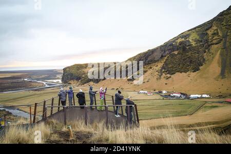 SKOGA, ISLANDA - 10 dicembre 2018: I turisti si trovano su una piattaforma panoramica a Skogafoss, guardando la cima della cascata dal punto panoramico. Foto Stock