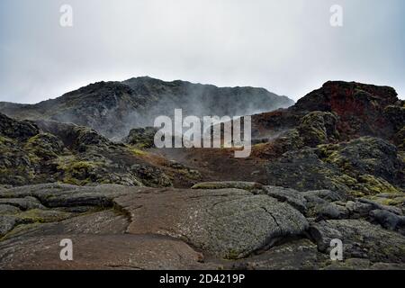 Il vapore sorge dai campi di Krafla Lava nell'area del Lago Myvatn, nel Nord dell'Islanda. Ossidazione rossa e muschio verde sono visibili sulla roccia vulcanica Foto Stock