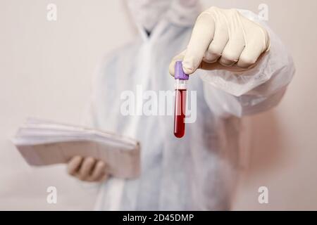 Mano con guanto in lattice per la fiala per campioni di sangue. Assistente di laboratorio maschio che tiene una provetta rossa con sangue su fondo bianco. Sangue, DNA e. Foto Stock