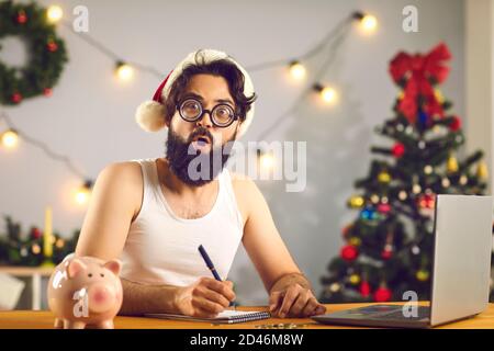 Uomo divertente seduto alla scrivania, scrivendo lettera a Santa o facendo la lista dei programmi e degli obiettivi per il nuovo anno Foto Stock