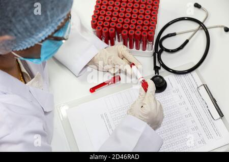 Il medico indiano esamina le fiale dei campioni di analisi del sangue dei pazienti durante la preparazione rapporto medico Foto Stock