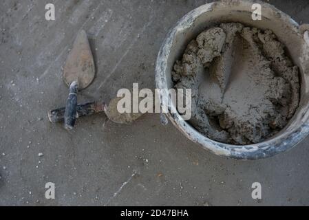 Cazzuola intonacata cemento misto in un secchio sul pavimento in cantiere Foto Stock