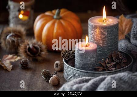 Concetto autunnale o celebrazione del Ringraziamento con due candele accese, zucca arancione sullo sfondo, castagne e coni di pino Foto Stock