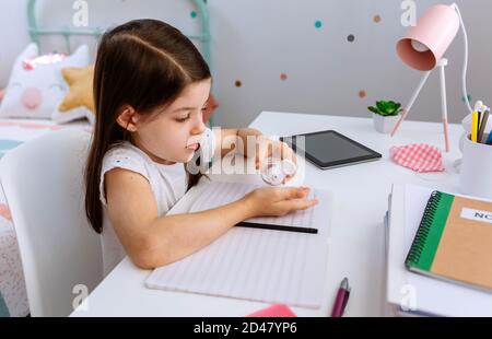 Ragazza che applica l'igienizzatore per le mani mentre fa i compiti Foto Stock