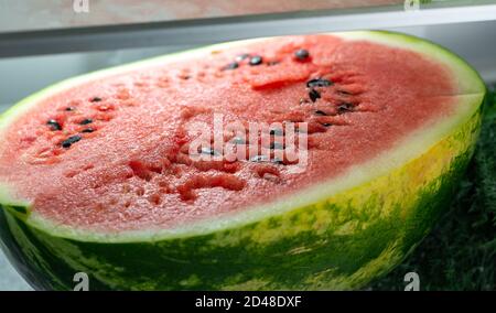 Metà di un cocomero su un piano di frigorifero. Carne rossa succosa e semi neri sono visibili. Cibo vegano. Foto Stock