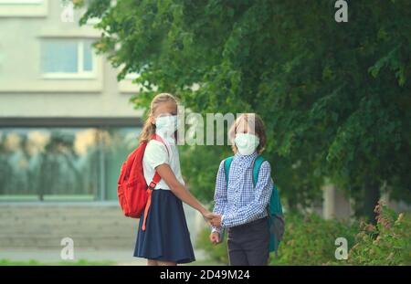 I bambini tornano a scuola. Simpatici alunni con zaini. Ragazzo e ragazza in maschere di sicurezza. Foto Stock