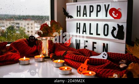 FELICE HALLOWEEN. Testo in scatola di luce bianca, con uno sfondo di maglione, foglie secche Halloween decorazione autunno sul davanzale. Finestra piovosa Foto Stock