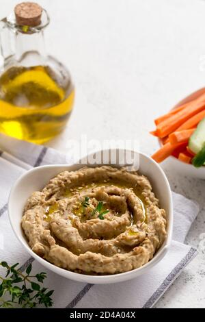 salsa di hummus in un recipiente, semi di sesamo, olio d'oliva, cetrioli e carote su sfondo chiaro Foto Stock