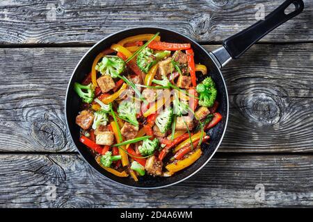 tofu kung pao con peperoni misti, broccoli e capesante in una padella su un tavolo rustico in legno, cucina cinese, vista del paesaggio dall'alto Foto Stock