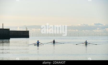 Brighton Regno Unito 9 ottobre 2020 - vogatori e scullers dallo Shoreham Rowing Club Godetevi una bella mattina serena e soleggiata al porto di Shoreham vicino a Brighton . Sullo sfondo la Fattoria del Vento di Rampion può essere vista all'orizzonte : Credit Simon Dack / Alamy Live News Foto Stock