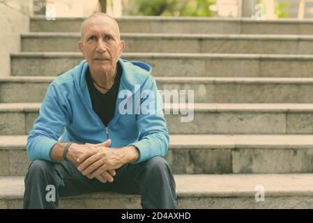 Bald senior uomo bracci pendente sulle ginocchia mentre è seduto sulla scala a Bangkok in Tailandia Foto Stock