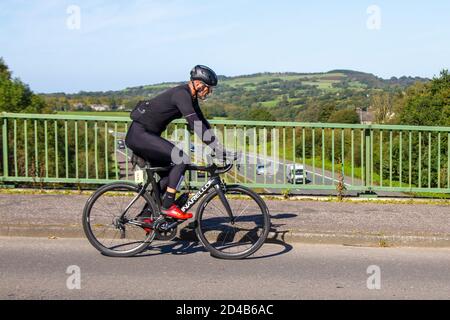 Ciclista maschile cavalcare nero Pinarello sport bici da strada sulla strada di campagna che attraversa il ponte autostradale nel Lancashire rurale, Regno Unito Foto Stock