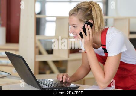 lavoratore femminile che indossa ungaree rosse utilizzando un computer portatile sul piano di lavoro Foto Stock