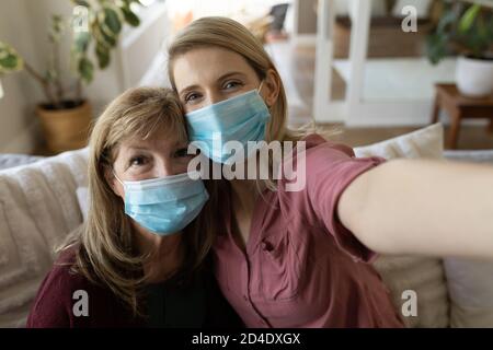 Donna anziana e sua figlia indossando maschera facciale prendendo selfie a casa Foto Stock