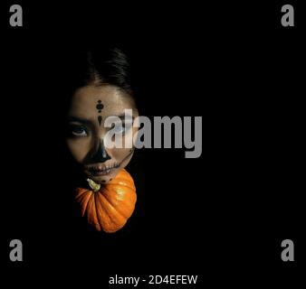 Giovane bella ragazza con trucco scheletro mettere la testa su una zucca su uno sfondo nero isolato. Il concetto della celebrazione di Halloween. Foto Stock