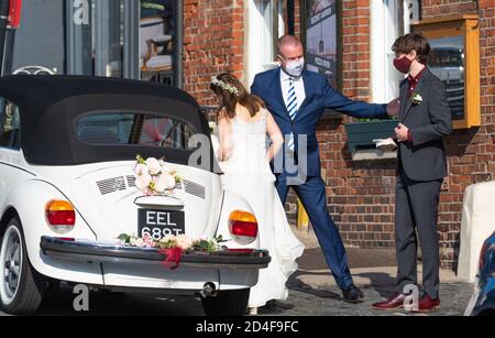 Una coppia che indossa maschere facciali che entrano in un'auto da sposa ad un evento sicuro COVID durante la pandemia di Coronavirus COVID19 nel Sussex occidentale, Inghilterra, Regno Unito. Foto Stock