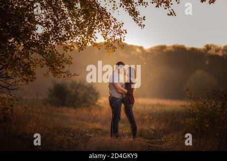 Un giovane e una donna camminano nella foresta autunnale. Gli amanti felici tengono le mani, si abbracciano, baciano, trascorrono il tempo insieme. Coppia in viaggio innamorata Foto Stock