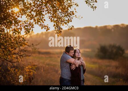 Gli amanti felici tengono le mani, si abbracciano, baciano, trascorrono il tempo insieme. Un giovane e una ragazza camminano nella foresta autunnale. Coppia in viaggio innamorata Foto Stock