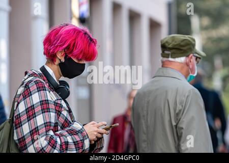 Riga, Lettonia - 8 ottobre 2020: Un giovane con i capelli rossi e una maschera medica sul viso è in attesa di trasporto pubblico per strada, mea preventiva Foto Stock