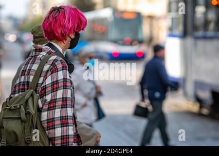 Riga, Lettonia - 8 ottobre 2020: Un giovane con i capelli rossi e una maschera medica sul viso è in attesa di trasporto pubblico per strada, mea preventiva Foto Stock