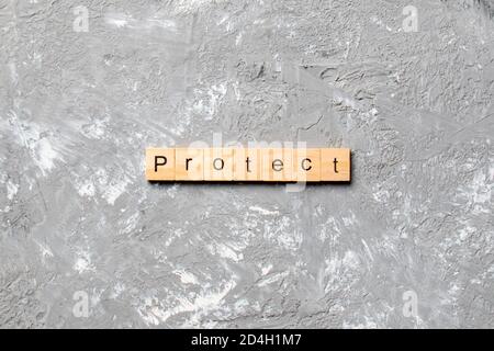 PROTEGGERE la parola scritta sul blocco di legno. PROTEGGA il testo sulla tabella di cemento per il vostro desing, concetto. Foto Stock