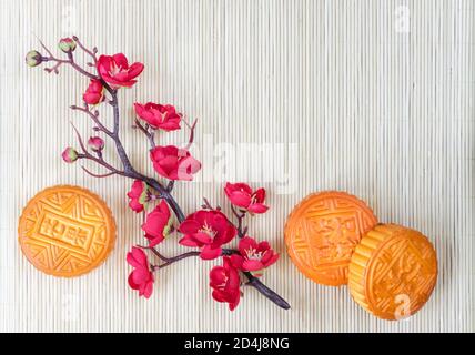 Composizione del festival cinese di metà autunno: Le tradizionali torte lunari cinesi e il ramo con fiori rossi sono su un tappetino di paglia, con spazio di copia Foto Stock