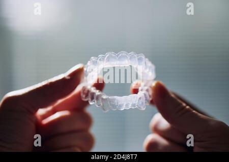 Vista ravvicinata dei denti di tenuta della mano che sbiancano i vassoi contro la finestra. Foto Stock