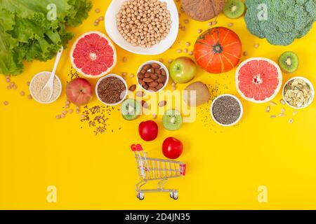 Carrello per lo shopping con verdure biologiche fresche, frutta e semi su sfondo giallo vista dall'alto Foto Stock